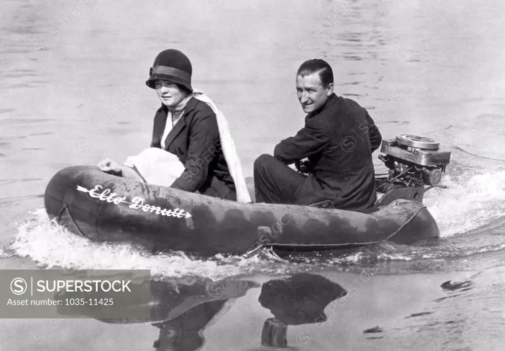 London, England: c. 1931. A happy English couple on an outing on the Thames. They are in a rubber lifesaving boat outfitted with an American outboard motor to push it along.©Underwood Archives