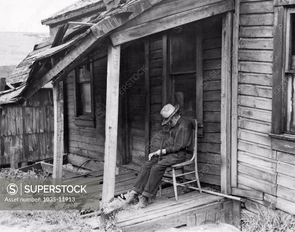 Washington, Pennsylvania:  1936. A very old man doses in a chair on the front  porch of a dilapidated shack of a home.