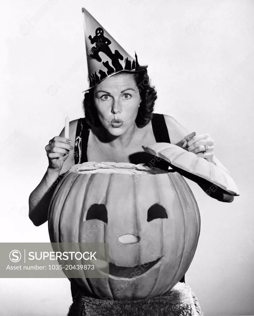 United States:  c. 1940 A woman looking scary with a pumpkin and a candle on Halloween.