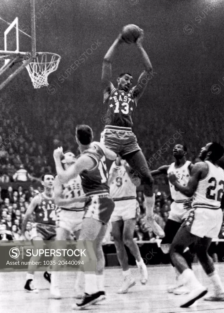 St. Louis, Missouri:  January 16, 1962 Wilt Chamberlain, Philadelphia (13), goes up high to snag a rebound in the NBA All-Star game. Below him are (l-r) Bob Cousey, Boston (14); Jerry West, Los Angeles (11); Tom Heinsohn,  Boston (15); Bob Pettit, St. Louis (9); Walt Bellamy, Chicago (8) and Elgin Baylor, Los Angeles (22).