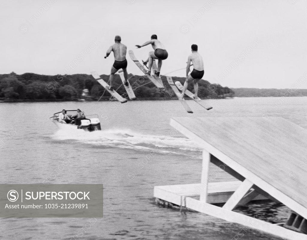 United States: c. 1956 Three members of the Min-Aqua Bats Waterski Club  take the jump simultaneously as part of the water ski show. - SuperStock