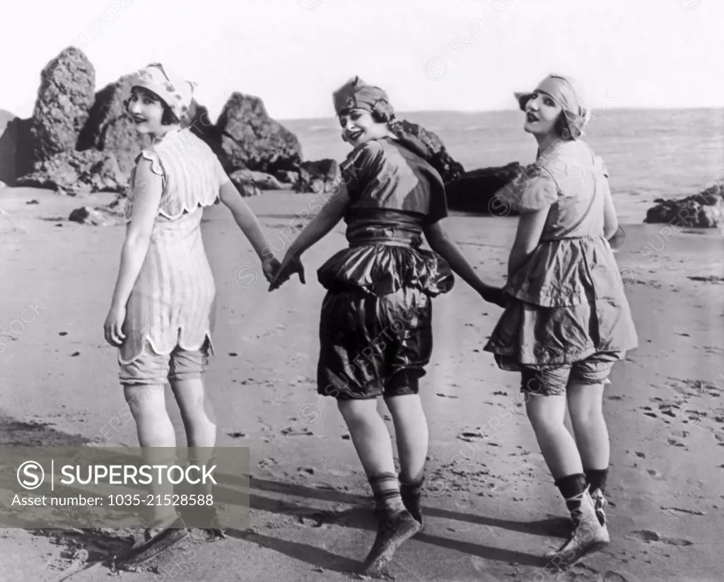 Los Angeles, California:  October, 1918 Silent film actresses Lillian Langston, Edith Roberts, and Myrtle Reeves, laughlingly pose holding hands on the beach.