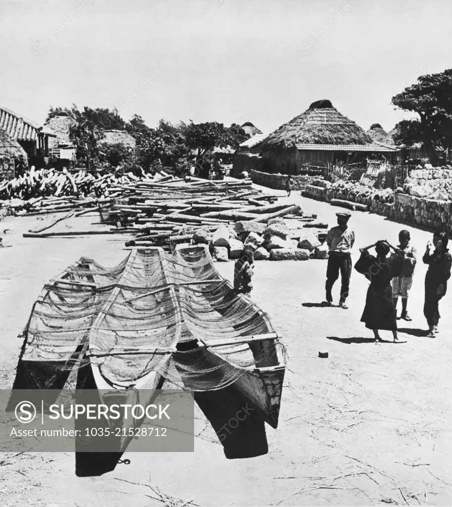 Okinawa, Japan:  May 21, 1945 A village on Okinawa with their fishing boats and nets in the foreground and the rocks and logs that they use to build their homes and huts piled in back.