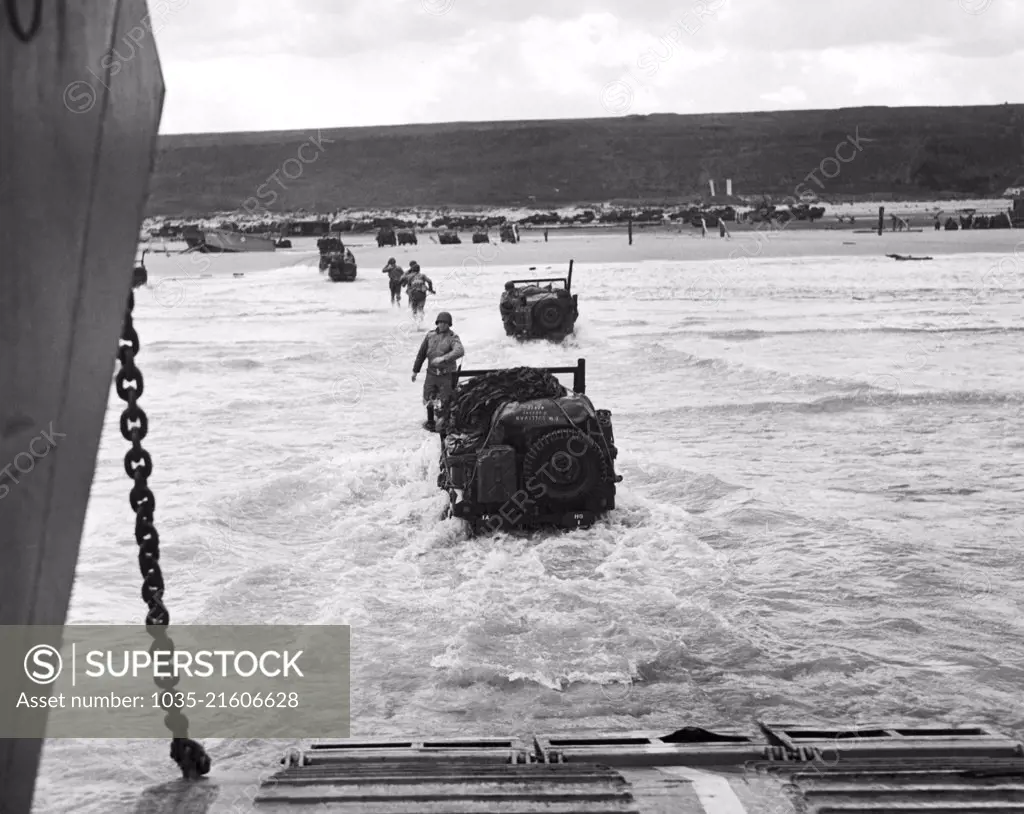 France: June 9, 1944 Allied soldiers make a run for the beach, followed by jeeps, as the invading forces are disgorged from transport vessels along the French coast.