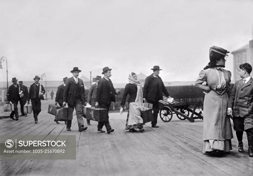 New York, New York:  c. 1895 Immigrants carrying their luggage as they arrivive at Ellis Island in NY harbor.