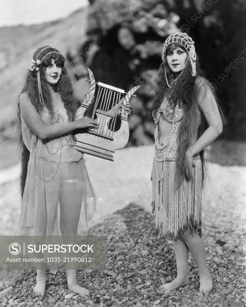 Hollywood, California,  c 1920. Two actresses in exotic dress pose with a beaded harp in a scene from an early silent movie.