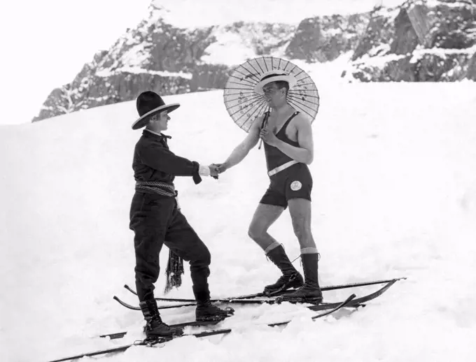 United States: c. 1923. A woman skier on the mountain slope wearing a sash and western hat shakes hands with a man on skis in a one piece bathing suit and carrying a parasol.