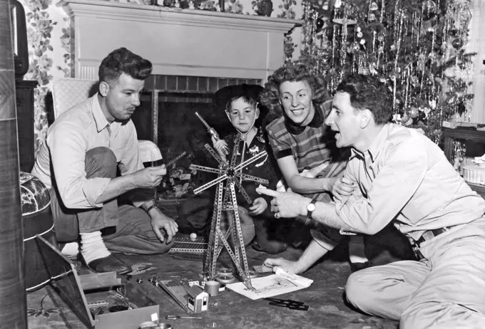 Millbrae, California:  c. 1954. A small boy dressed in a cowboy outfit watches as his parents and friend play with the erector set that he got for Christmas