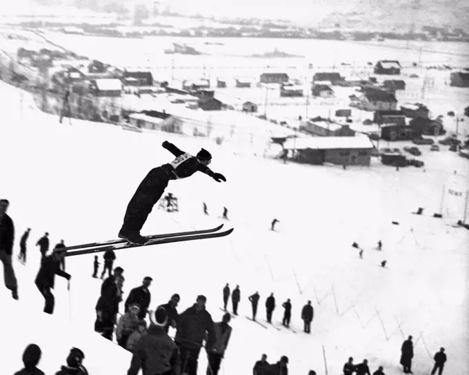 United States:  c. 1957. A skier takes off the in the air and shows great form in this winter scene.