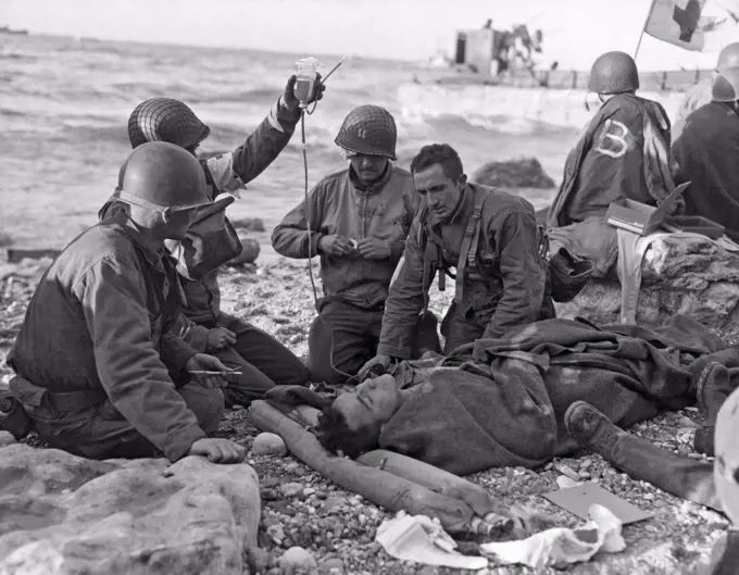 Normandy, France:  June 7, 1944. Medics gving plasma on the beach to a wounded survivor of a sunken landing craft during the Normandy invasion.