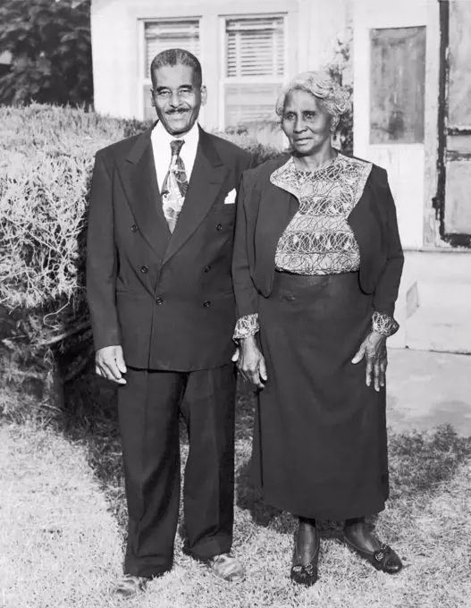 United States:  c. 1938 An older African American man and his wife pose for a portrait outside their home.