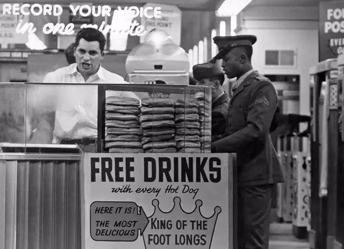 San Francisco, California  c. 1950. The vendor at  the foot-long hot dog stand at Playland At The Beach in San Francisco. An African American soldier stands in line.