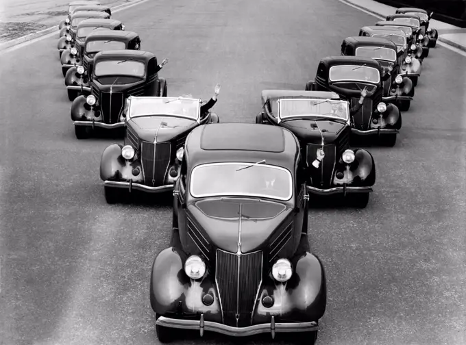 United States: c. 1934 A fleet of fifteen Cadillacs driving down the street in a 'V' formation.