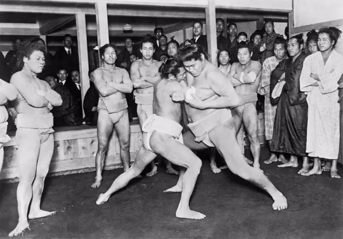 Japan:  c. 1924 Japanese sumo wrestlers competing in a match while other wrestlers and spectators watch.