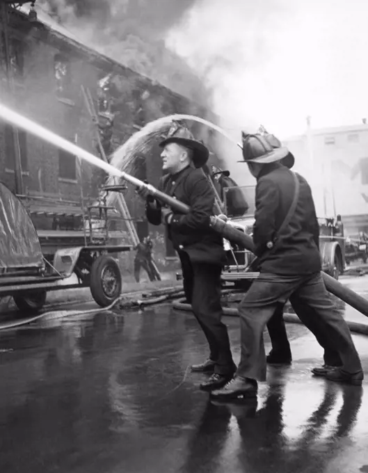 Chicago, Illinois:  c. 1935 Three firemen directing a hose at a large building on fire.