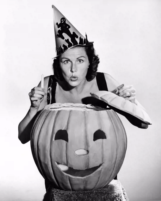 United States:  c. 1940 A woman looking scary with a pumpkin and a candle on Halloween.