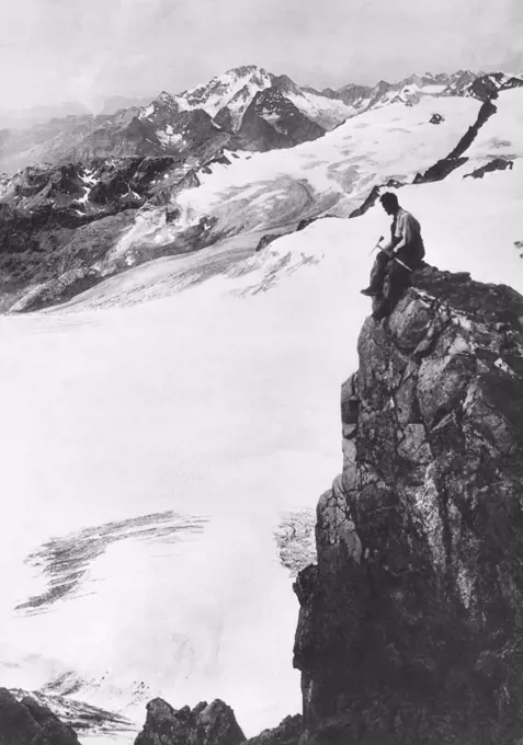 Canada:  c. 1930 A mountain climber sits on a precipice overlooking the snow covered valleys below