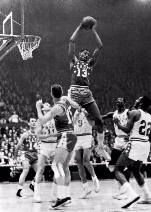St. Louis, Missouri:  January 16, 1962 Wilt Chamberlain, Philadelphia (13), goes up high to snag a rebound in the NBA All-Star game. Below him are (l-r) Bob Cousey, Boston (14); Jerry West, Los Angeles (11); Tom Heinsohn,  Boston (15); Bob Pettit, St. Louis (9); Walt Bellamy, Chicago (8) and Elgin Baylor, Los Angeles (22).
