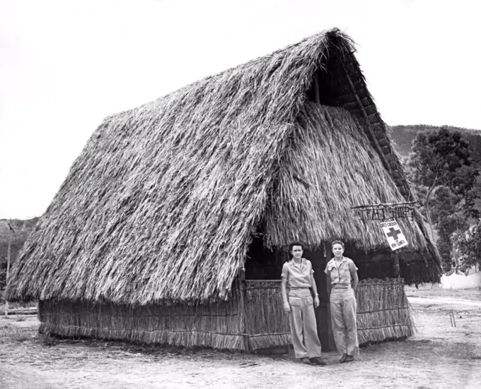 New Guinea:  c. 1944 Two nurses stand in front of their thatched hut Red Cross shelter in New Guinea during World War II.