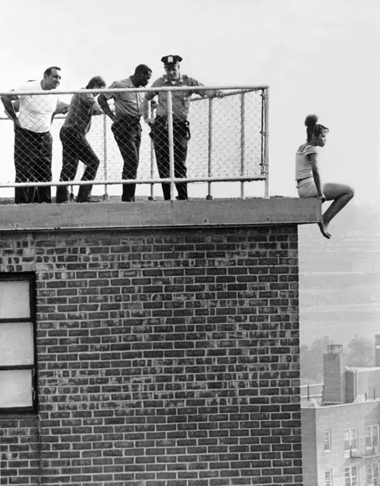 New York, New York:  June, 1972 New York City police try to look nonchalant as they try to talk a young woman into refraining from jumping from the 15th floor ledge she is perched upon.