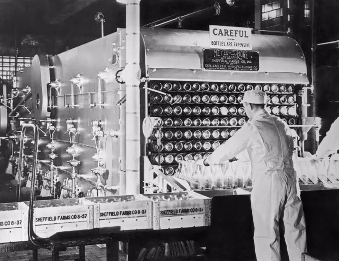 New York, New York:  c. 1926 A Sheffield Dairy Farms employee working at the milk bottle washing machine during the sterilization process at their New York City plant. Above him is a sign admonishing, "Careful. Bottles Are Expensive".