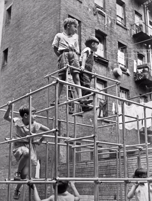 New York, New York:  c. 1935. Children playing in the first of the Tot Lot playgrounds in New York City. The doors are only 42 inches high, and in the shape of a small girl dancing, so only young children cam squeeze in. This one is on West 49th St between 9th and 10th Avenues.