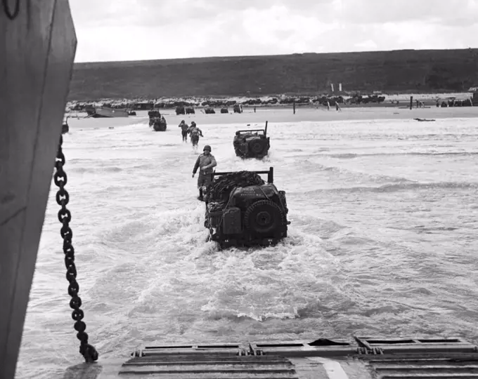 France: June 9, 1944 Allied soldiers make a run for the beach, followed by jeeps, as the invading forces are disgorged from transport vessels along the French coast.