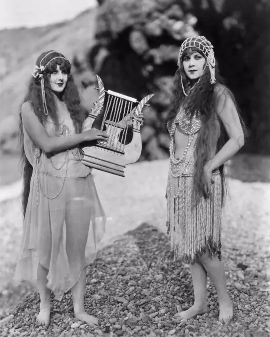 Hollywood, California,  c 1920. Two actresses in exotic dress pose with a beaded harp in a scene from an early silent movie.