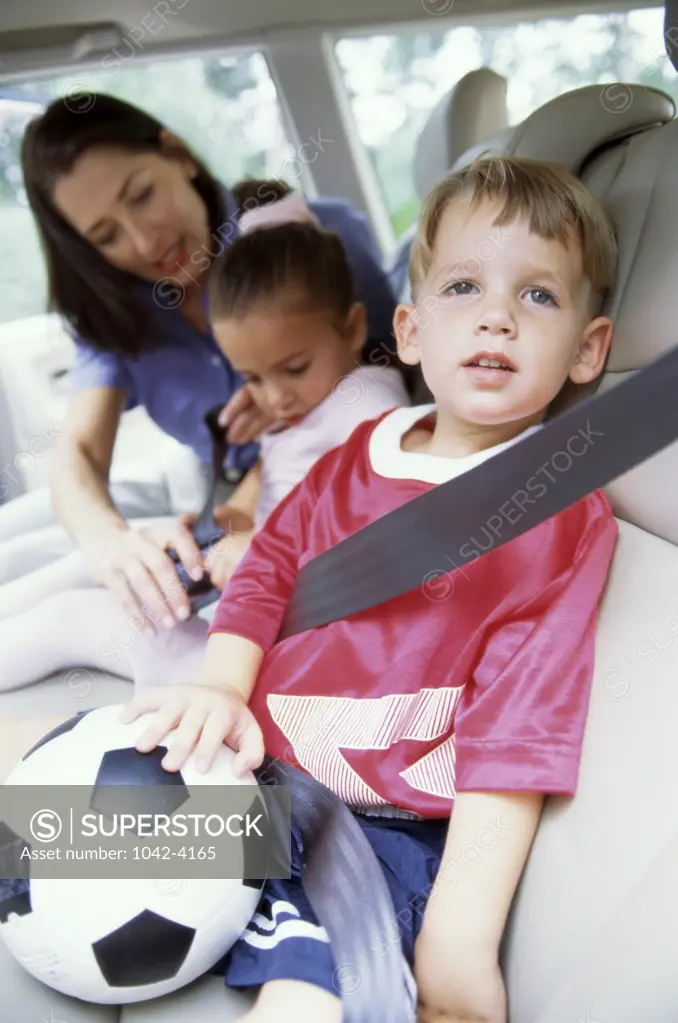 Mother strapping in her son and daughter in the car