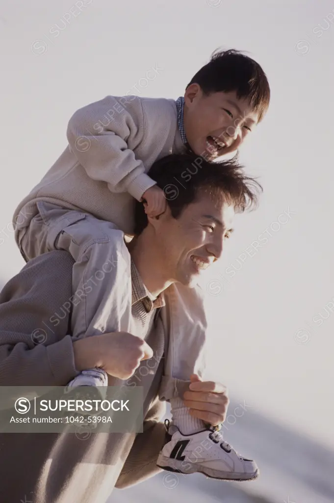 Close-up of a young man carrying his son on his shoulders and smiling