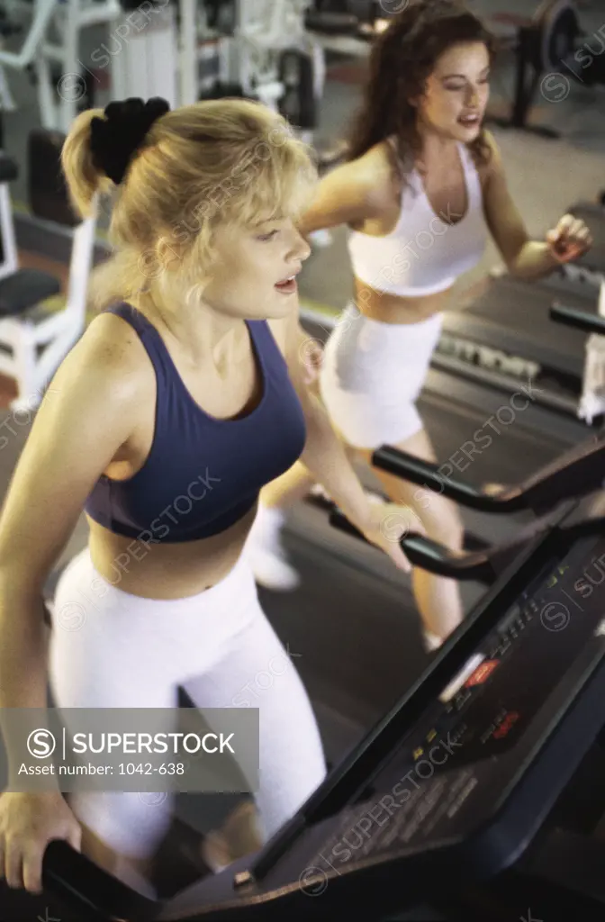 High angle view of two young women running on treadmills in a gym