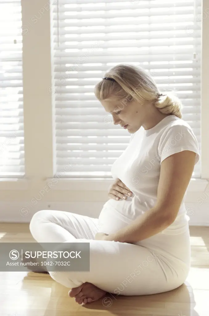 Pregnant woman sitting on the floor touching her abdomen