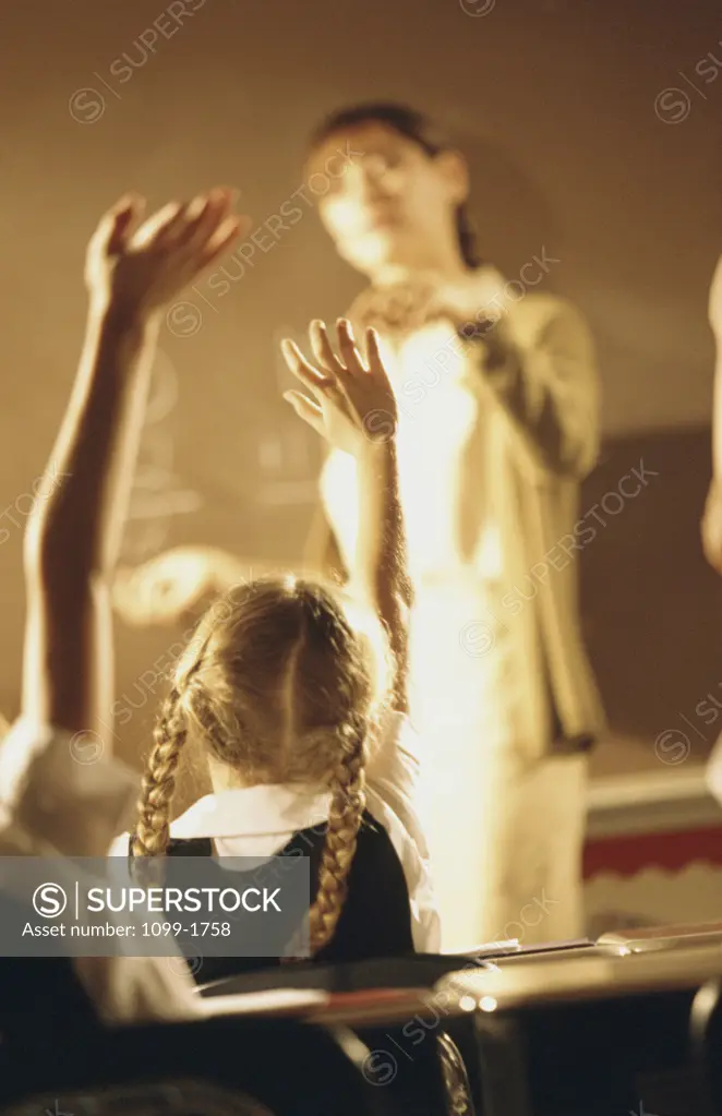 Rear view of a schoolgirl sitting with her hand raised in a classroom