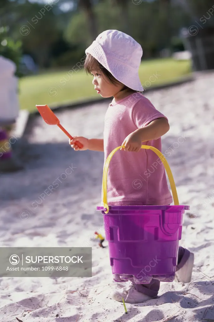 Side profile of a girl carrying a sand pail and a shovel