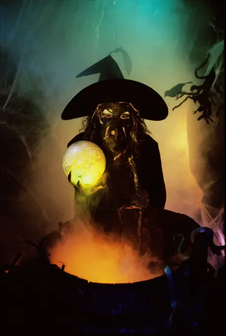 Witch holding a crystal ball standing in front of a cauldron