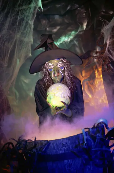 Witch holding a crystal ball standing in front of a cauldron