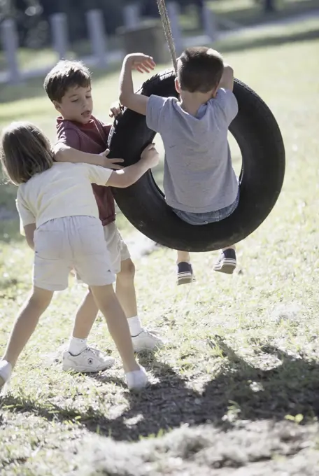 Two boys and a girl paying on a tire swing