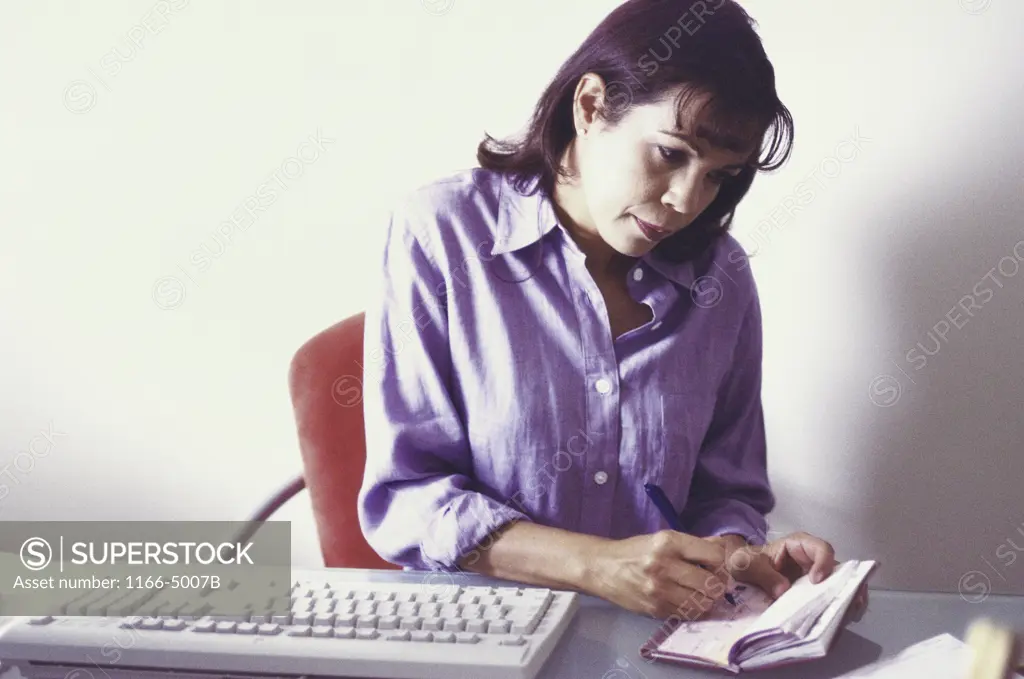 Mid adult woman sitting and writing a check in an office