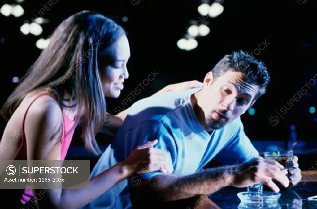 Close-up of a young woman sitting with a drunk young man at a bar