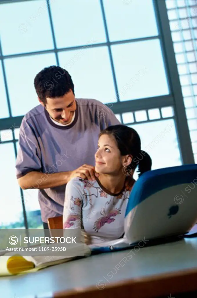 Teenage girl using a laptop with a teenage boy standing behind her