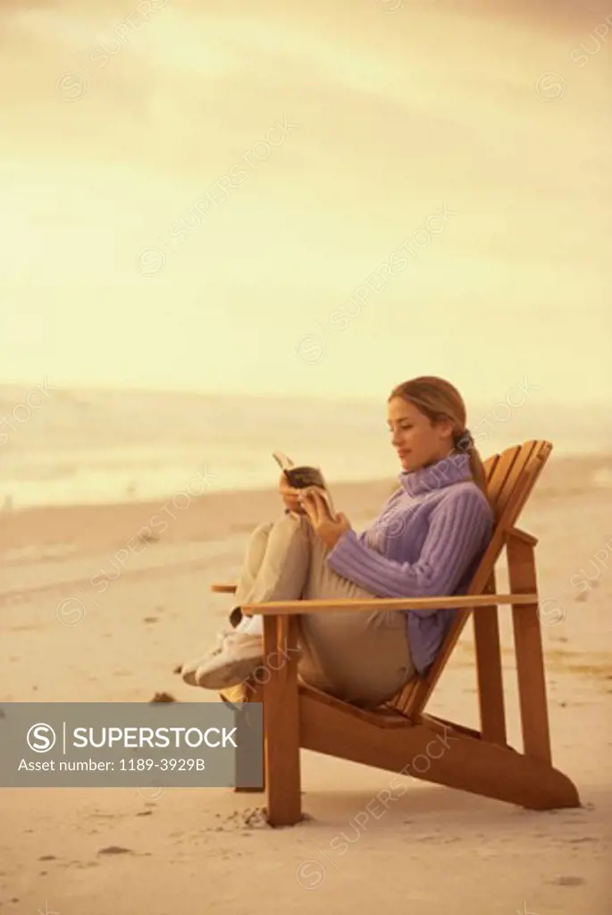 Side profile of a young woman reading a book on the beach