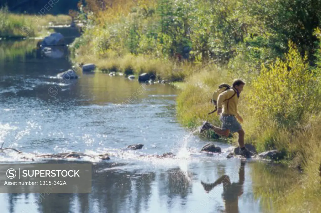 Side profile of a view of a young man running across a river