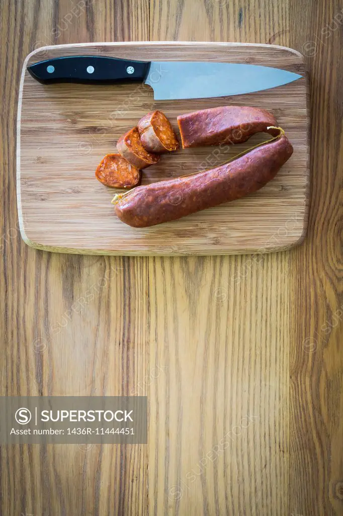 Chorizo Sausage cut into pieces on a wooden cutting board with knife next to it.