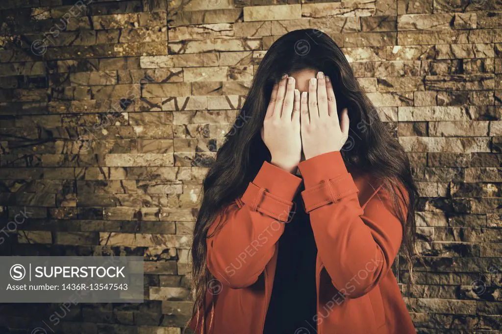 Scared teenage girl hiding face with hands crying.