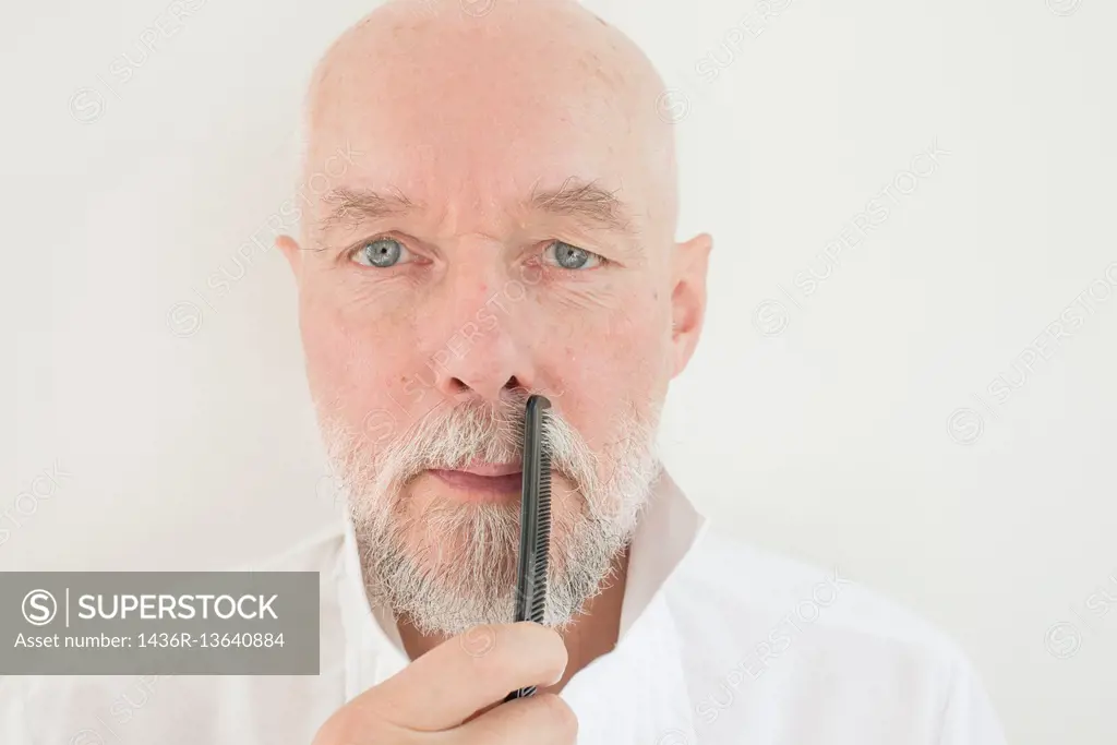 Old man combing beard and mustache with comb. Serious senior adult taking care of his facial hair.