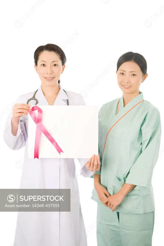 Female doctor and young woman in examination gown showing board of pink ribbon