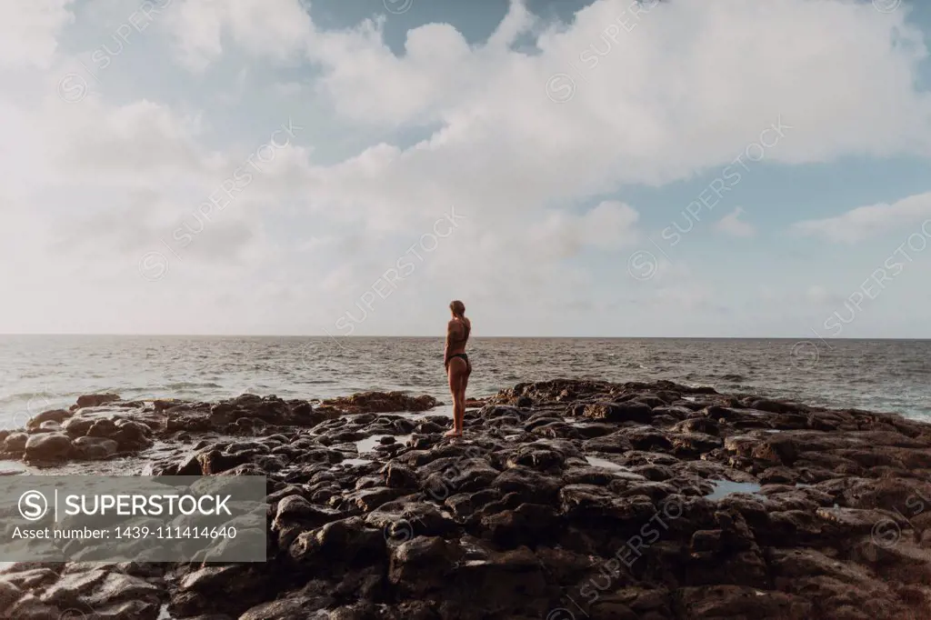 Swimmer standing on rocks by sea, Princeville, Hawaii, US