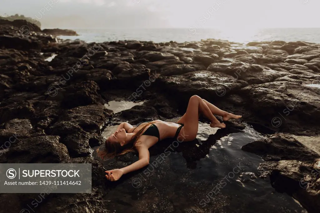 Woman lying on rocks by seaside, Princeville, Hawaii, US