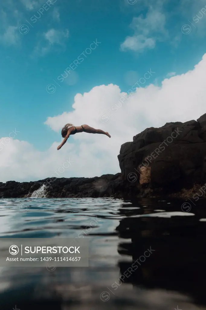 Swimmer diving off rocks into sea, Princeville, Hawaii, US