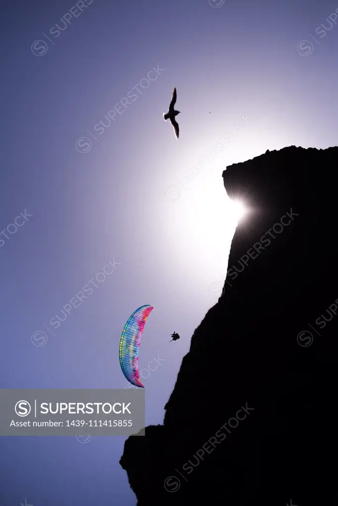 Paraglider gliding mid air near cliff against blue sky, Vik, Iceland